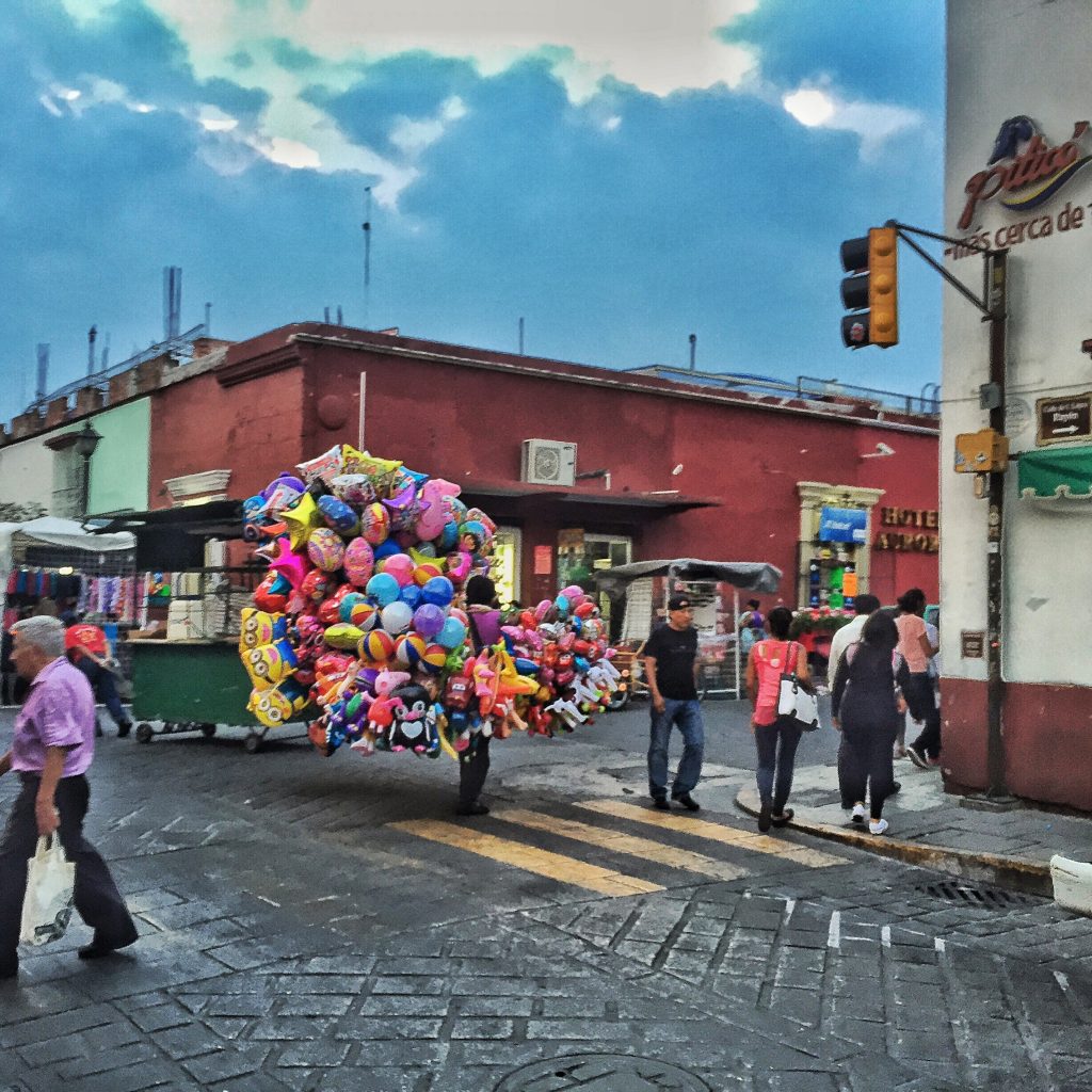Balloon guy battles brisk winds and narrow streets en route to the zocalo to sell balloons to families.